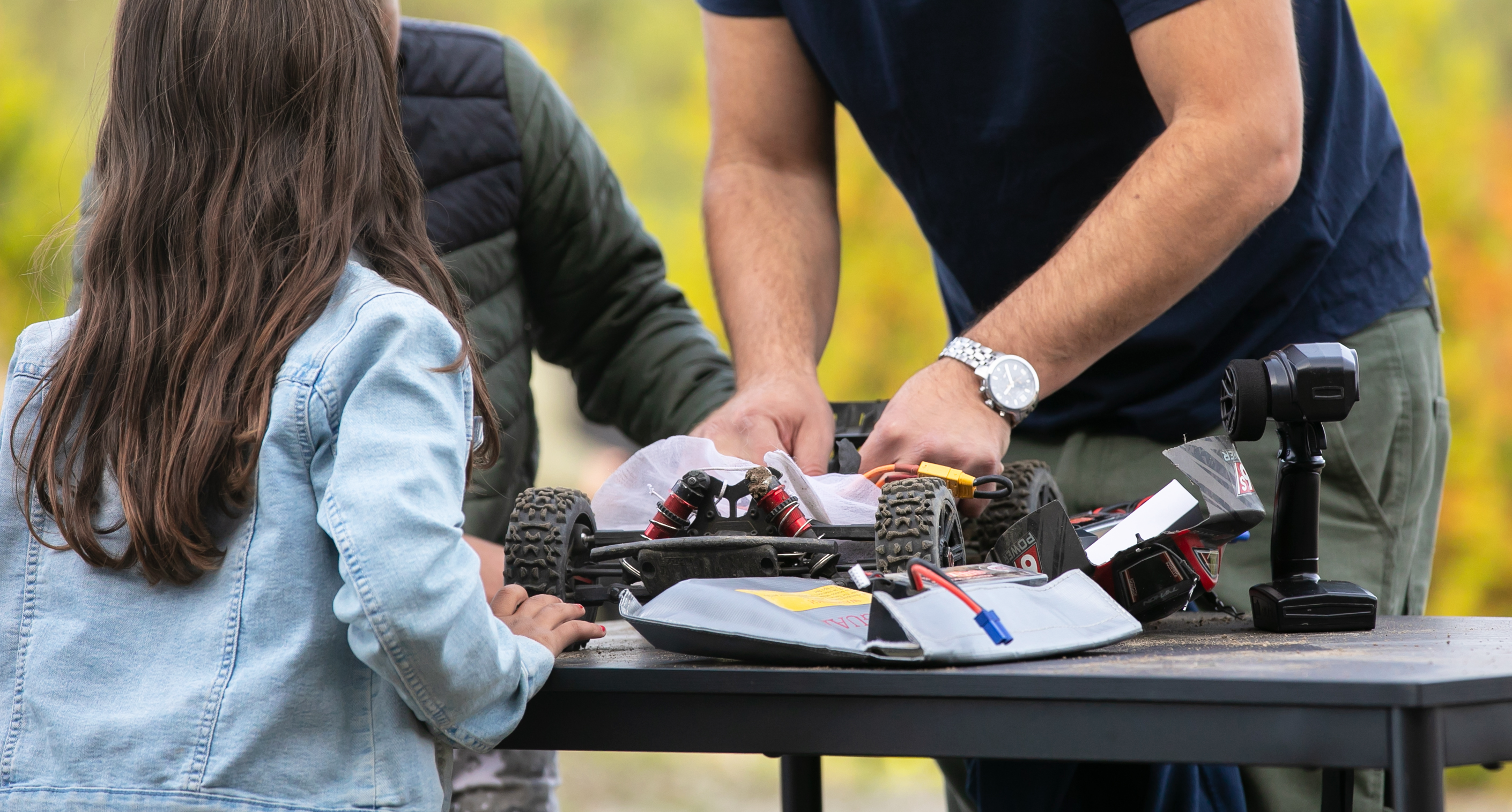 Pappa som mekar med en RC-bil med två barn som tittar på