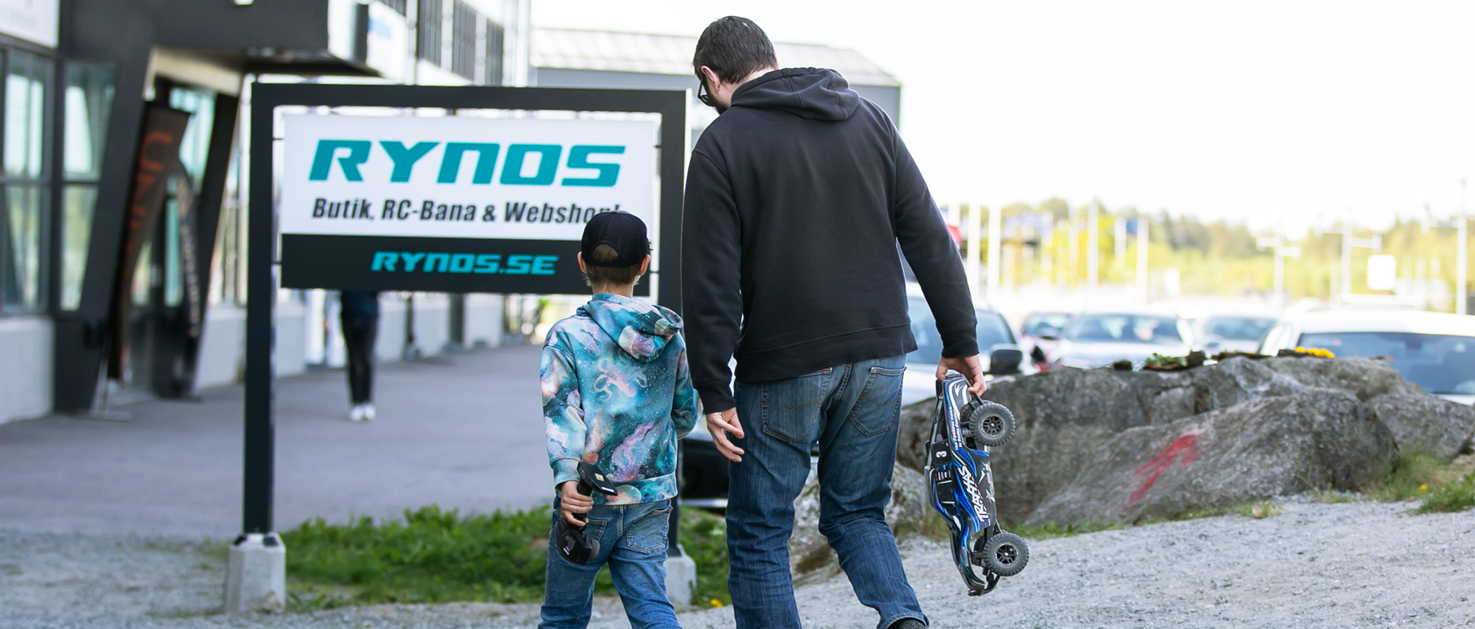 Far och son går bredvid varandra vid en skylt vid Rynos RC-bana och butik